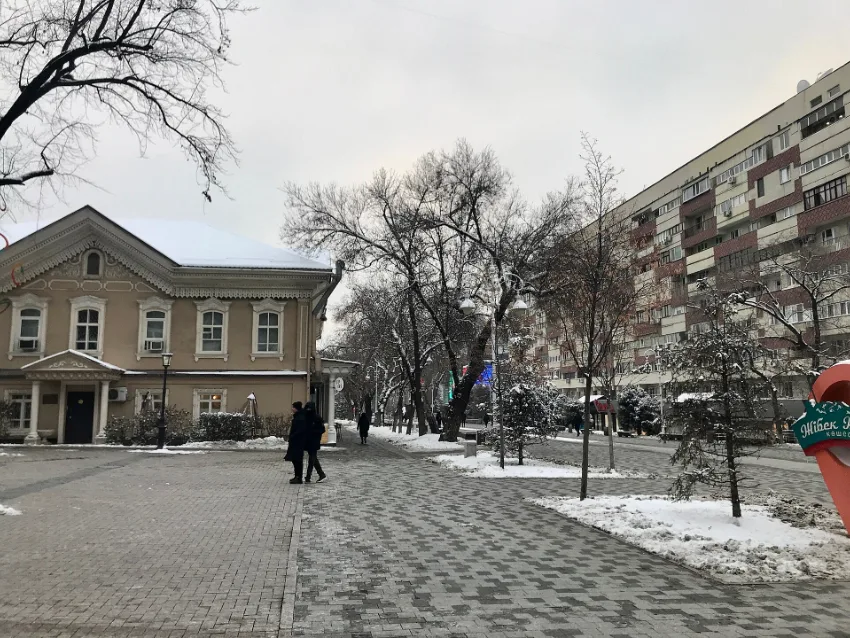 Jalan pejalan kaki Arbat di Almaty dengan pokok tanpa daun dan salji nipis di tepi jalan pada akhir November